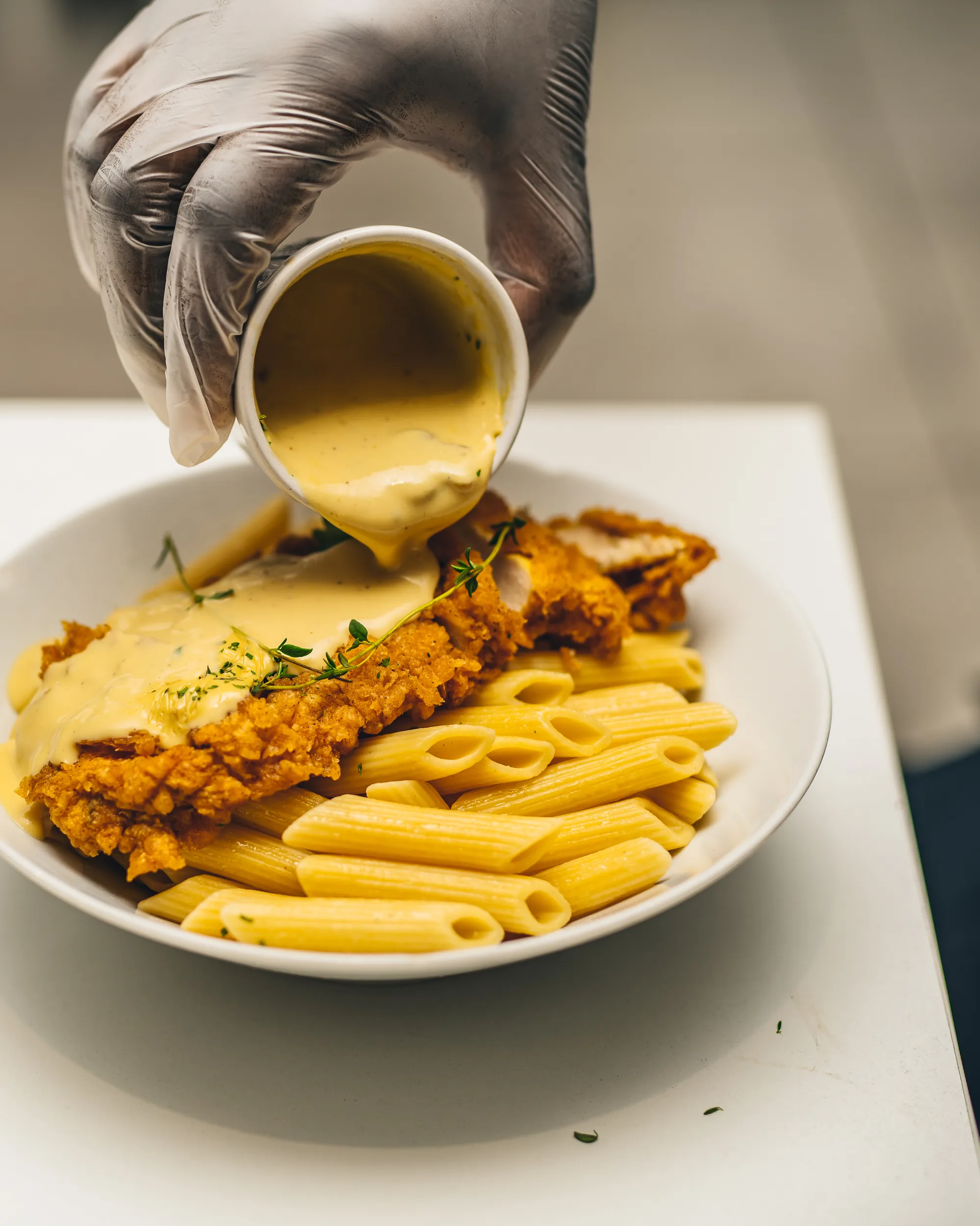 Chef finishing breaded chicken and penne with a creamy sauce, Italian private catering in London